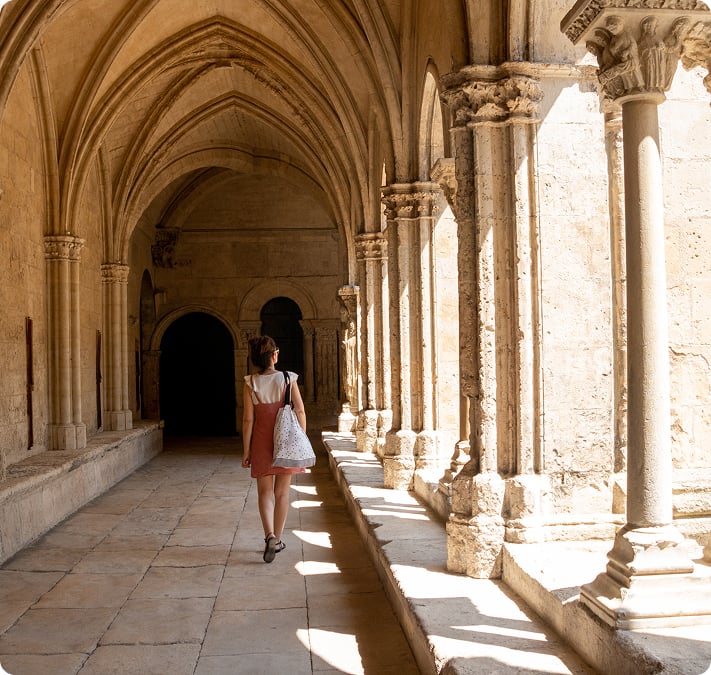 Une voyageuse marchant sous les arcades d'un cloître roman