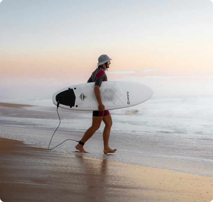 Un surfeur, planche sous le bras, marchant au bord de l'eau au coucher du soleil