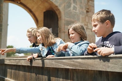 Trois enfants penchés sur une balustrade en bois, sous une arche en pierre