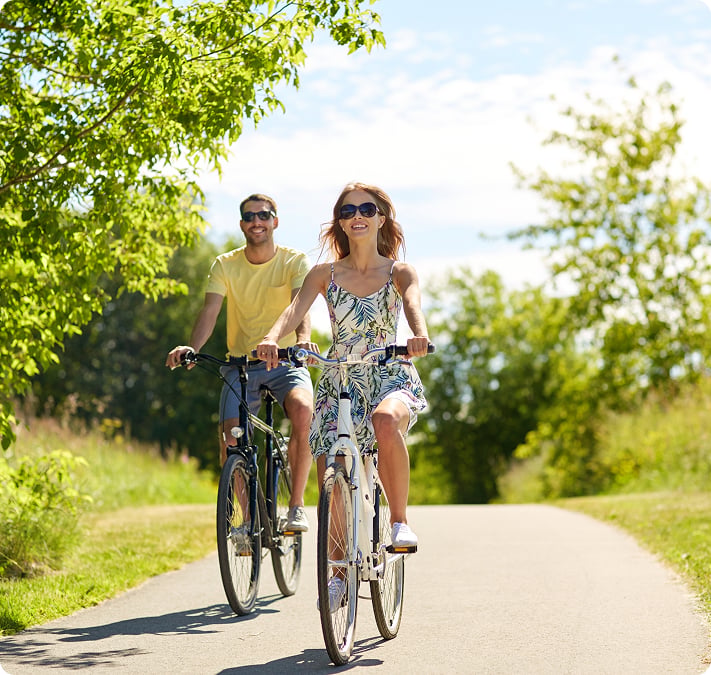 Un couple à vélo sur une voie verte bordée d’arbres