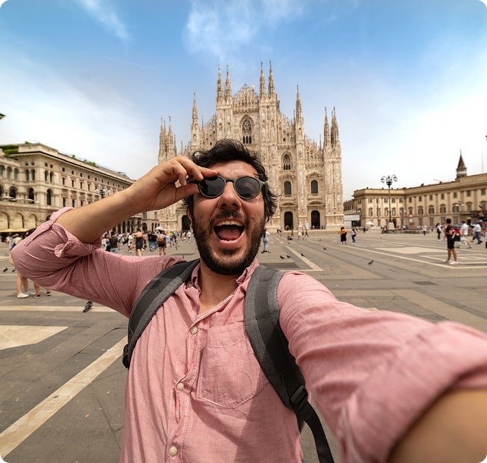 Un voyageur souriant prenant un selfie devant le Duomo de Milan
