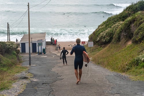 Un surfeur, planche sous le bras, descendant vers une plage de Saint-Jean-de-Luz