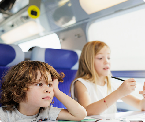 Deux enfants installés à une tablette dans un TGV INOUI, en train de dessiner pendant le trajet.